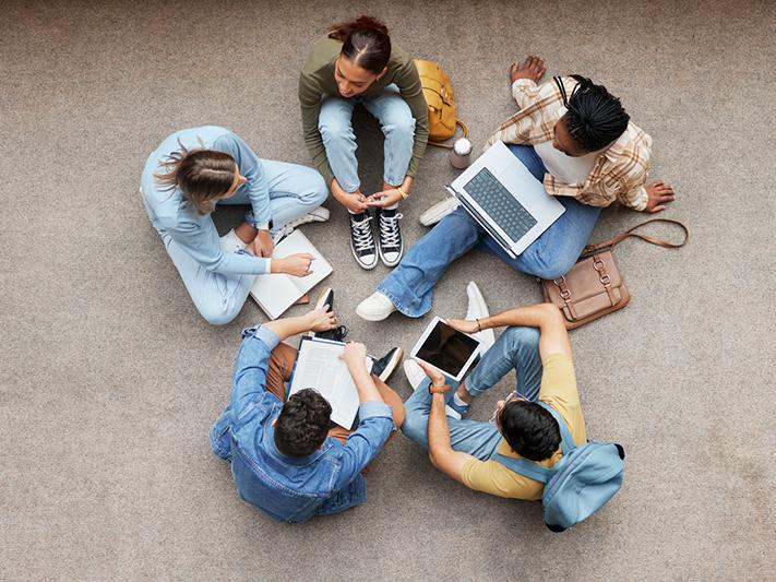 Students sitting in a circle on the floor with laptops