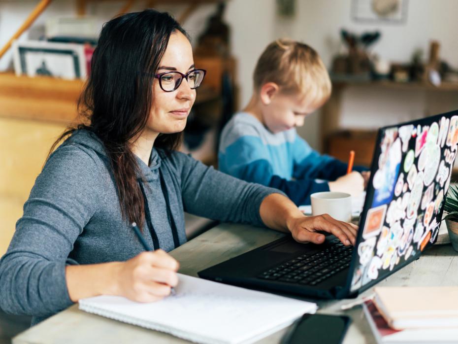 A mother on her laptop while her son plays next to her