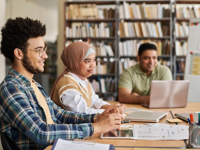 University students at a desk surrounded by shelves full of books