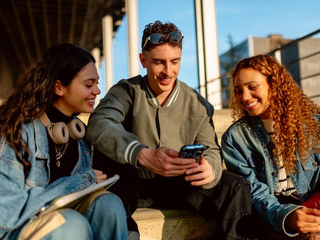 University students sitting outside looking at a funny video on one of their phones