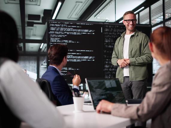 A team of coders brainstorming in front of a large code-filled screen