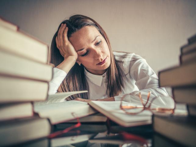 An academic surrounded by books looks stressed