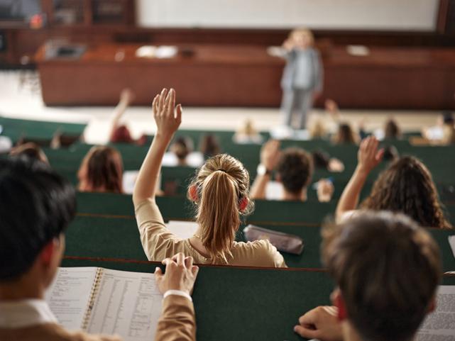 A student raises a hand in a lecture hall
