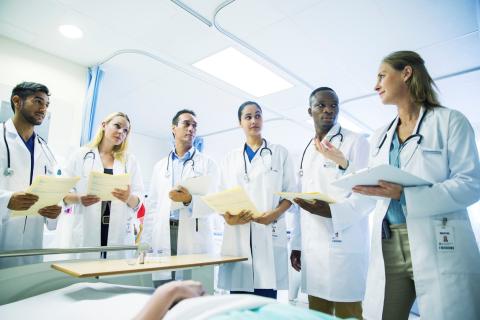 A group of medical students stand around a patient in bed