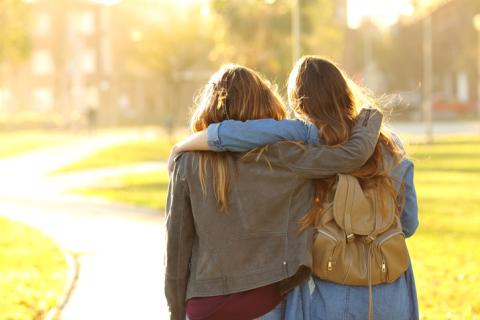 Two women walk away from the camera, their arms around each other's shoulders