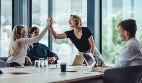 A manager high-fives a member of staff around a meeting room table