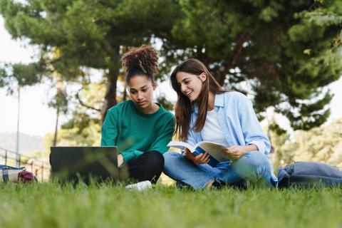 Two students stitting outside on the grass with their laptop and text books