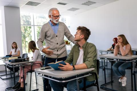 A lecturer speaking to a student at their desk