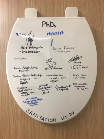 A toilet seat featuring the signatures of PhD students