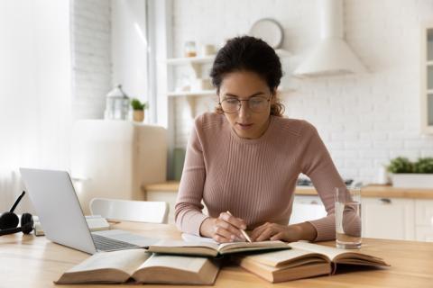 A woman works on an essay, using her laptop and several books