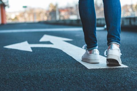 A pair of legs following an arrow on asphalt