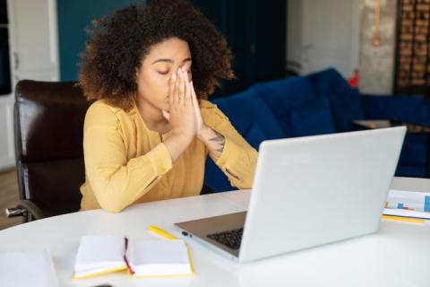 A young woman takes a deep breath at a laptop