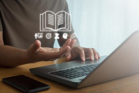 A virtual illustration of a book guides a student working on a laptop