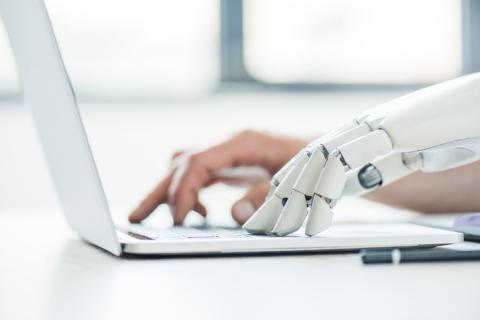 A robot hand types at a laptop