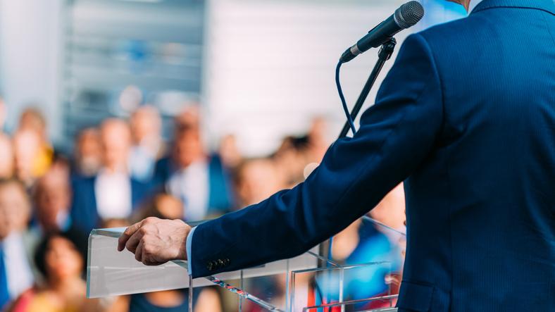 A speaker stands at a lectern with a microphone