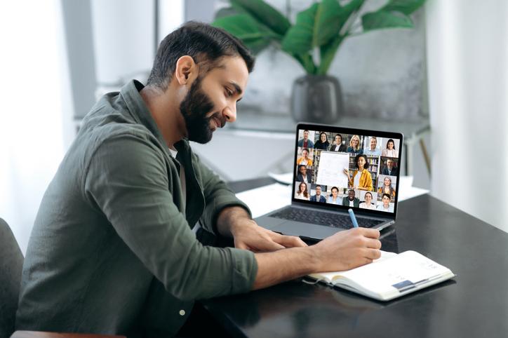 A man takes notes as he watches an online lecture on his laptop