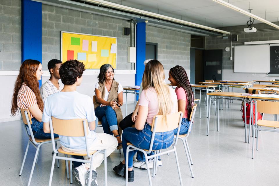 A group of students sitting in a circle while a teacher addresses them