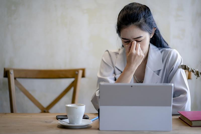 Young Asian woman looking tired at laptop