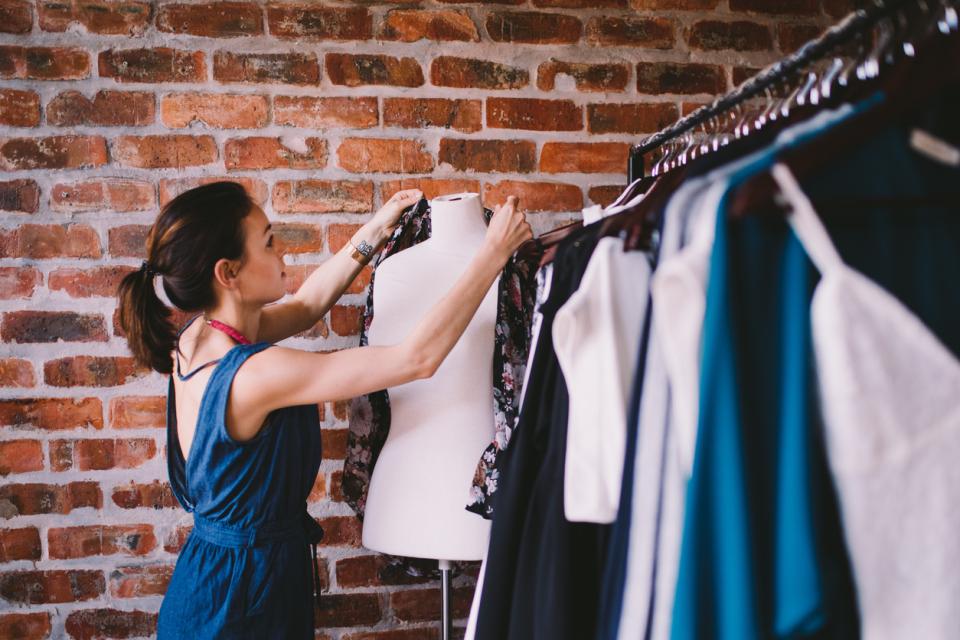 A woman putting a shirt on a mannequin next to clothes rails