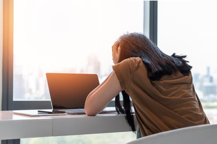 A woman holds her head in her hands over a laptop screen