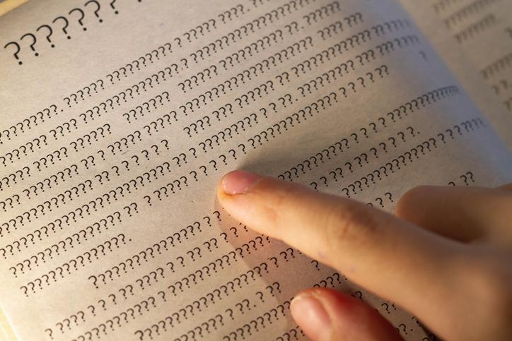 A finger follows text in a book written in question marks