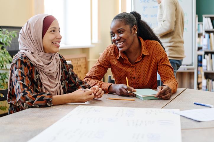 Two women laugh together over a notebook