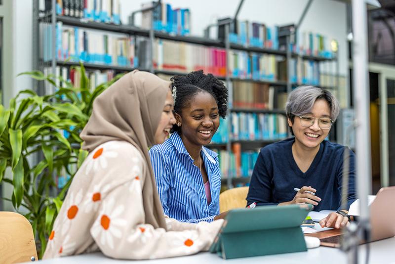 Three young multiracial female scholars in library