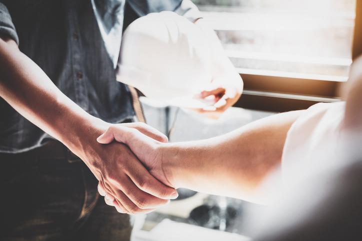Two people, one carrying a hard hat, shake hands