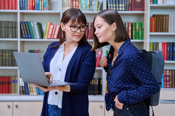 A librarian helps a student, using a laptop