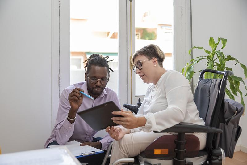 Woman in wheelchair and young black man looking at tablet