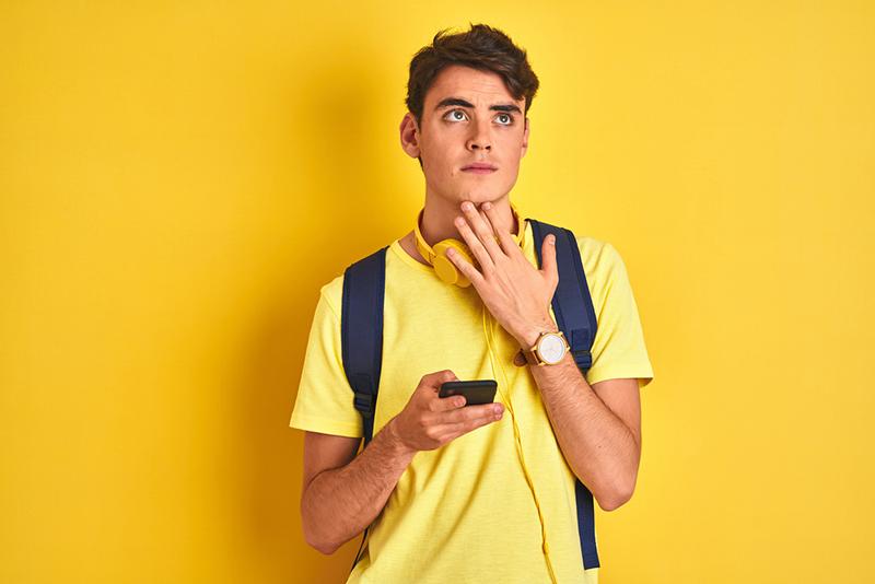 Young male student looking perplexed with mobile phone