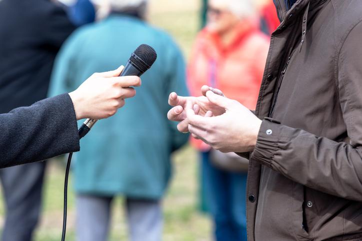 A journalist interviews a man in a raincoat