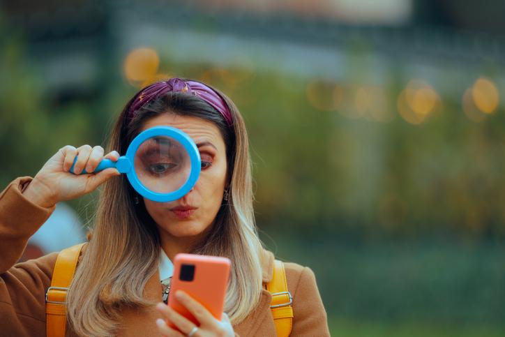 A woman uses a magnifying glass to check her phone