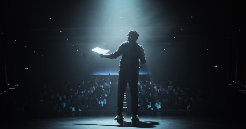 A lecturer is illuminated by the stage lights