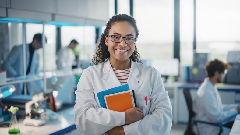 A student in a lab coat smiles