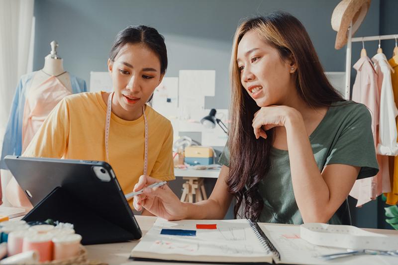 Two female Asian fashion design students in workshop