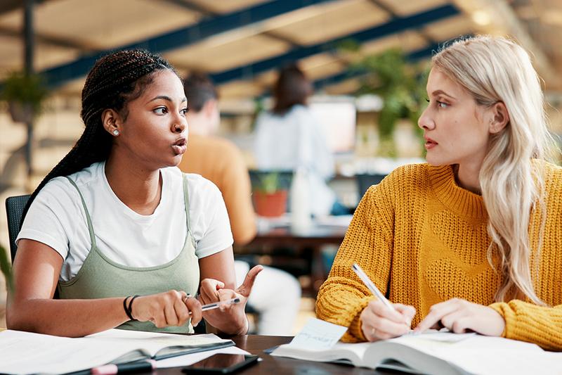 Two young female college students talking in library