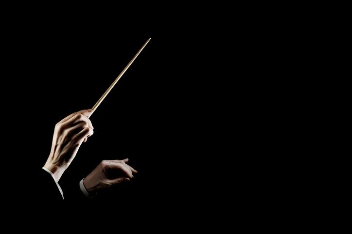 A conductor gestures with a baton against a black blackground