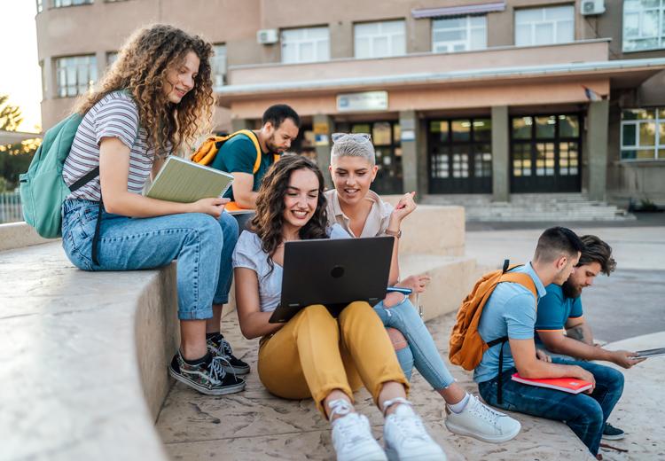 A group of students on campus using laptops and mobile devices
