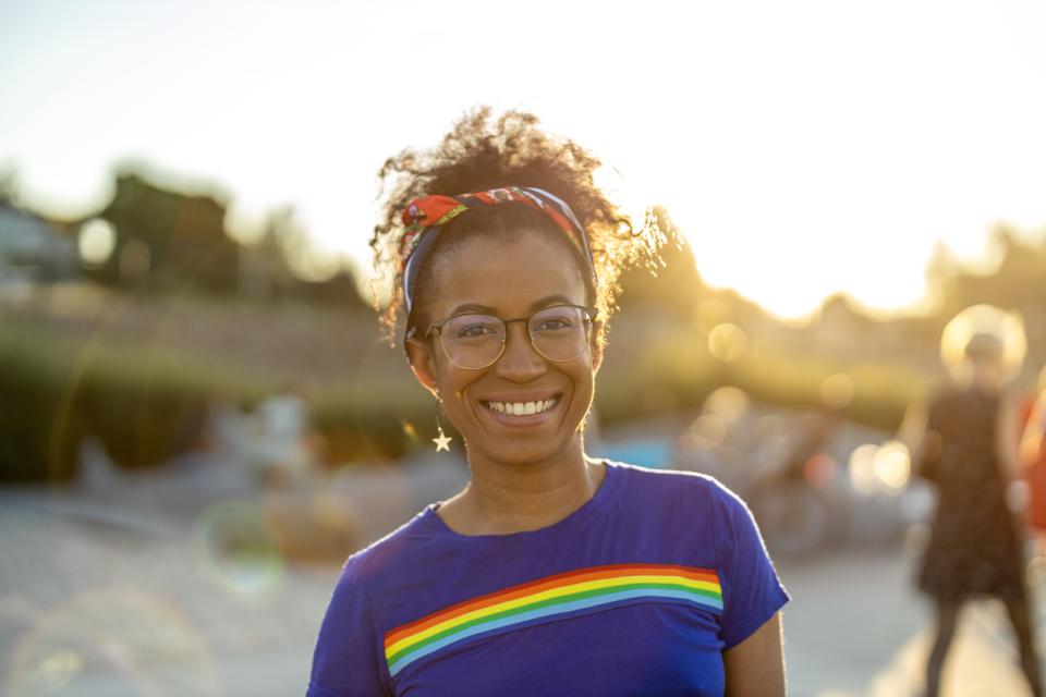 A young woman smiling to camera ourside wearing a t-shirt with a rainbow on it