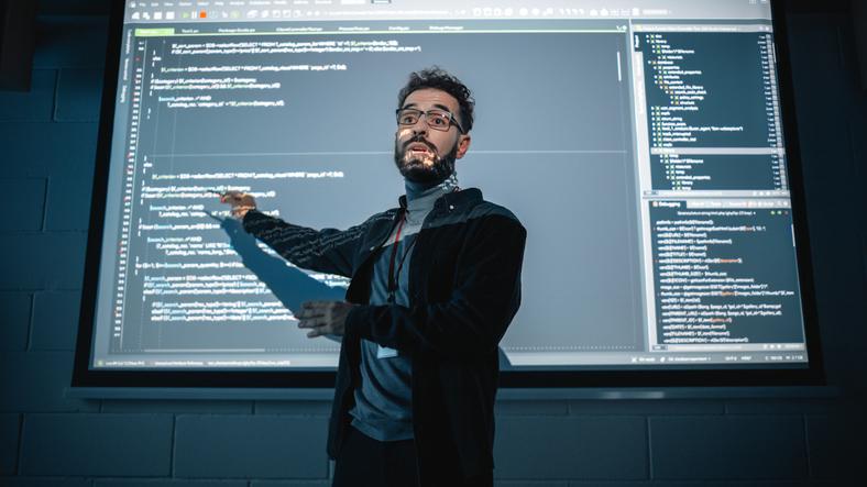 A teacher stands in front of a projector screen