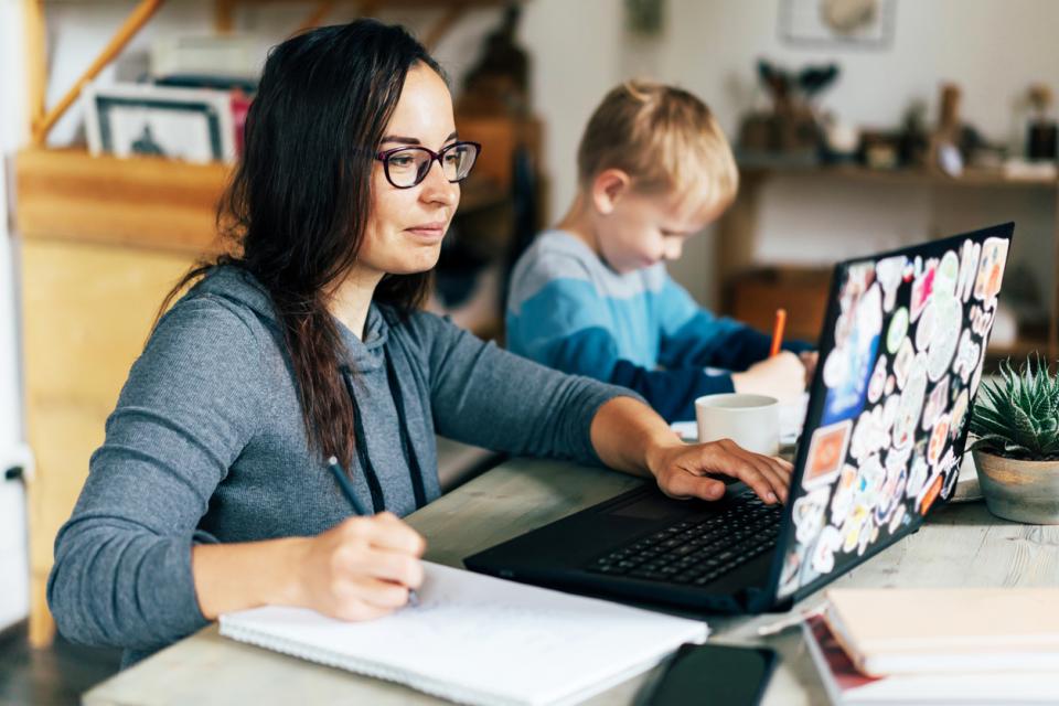 A mother on her laptop while her son plays next to her