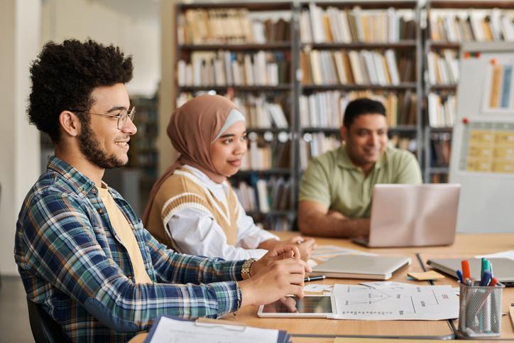 University students at a desk surrounded by shelves full of books