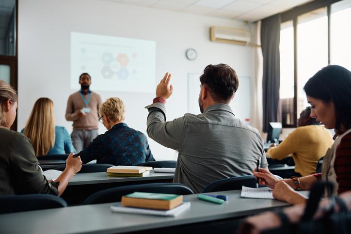  Back view of student raising his hand to answer teacher's question 
