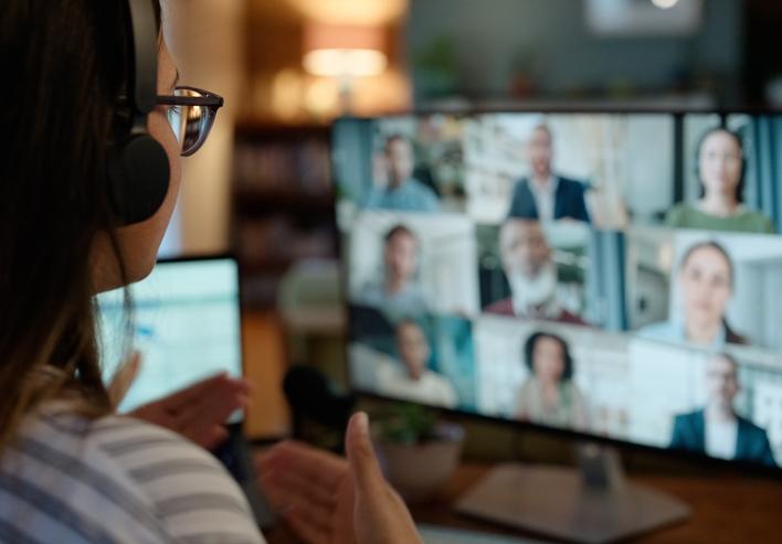 A student wearing headphones speaking to a screen with other students online