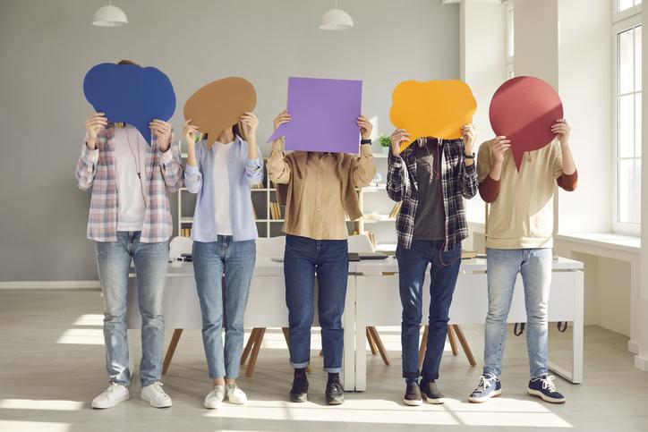 Students hold brightly coloured speech bubbles up to their faces