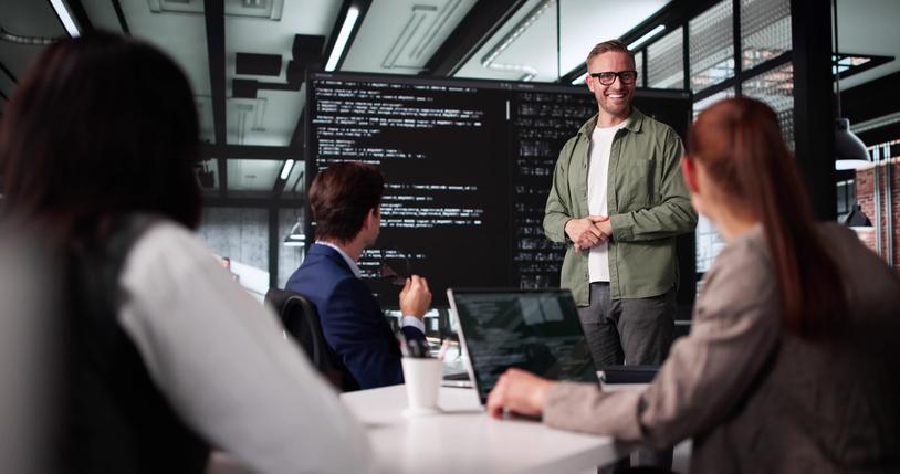 A team of coders brainstorming in front of a large code-filled screen