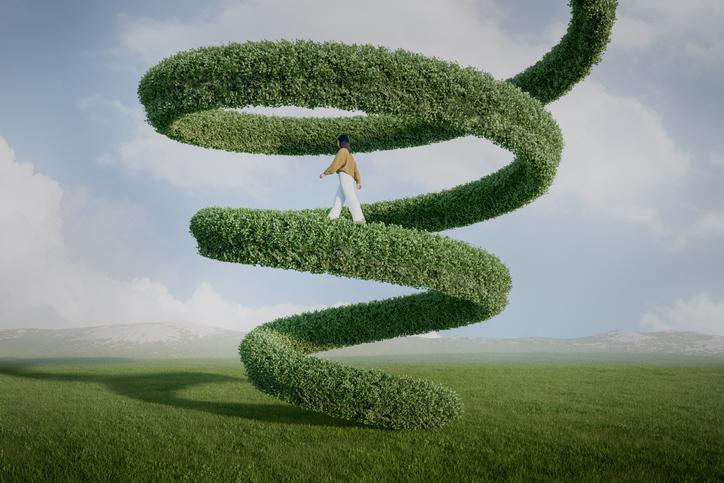 A woman walking up a leafy green structure extending up into the sky