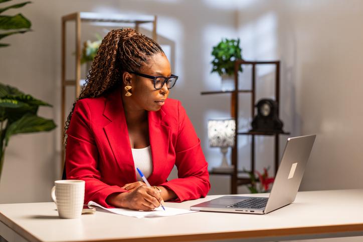 A Black female academic with glasses sat at a desk on her laptop