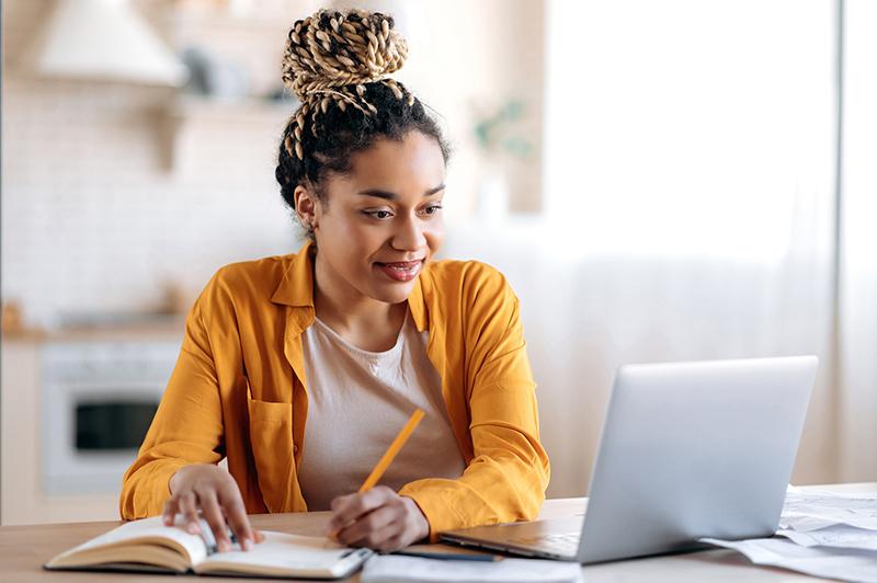 Black female student taking notes at laptop
